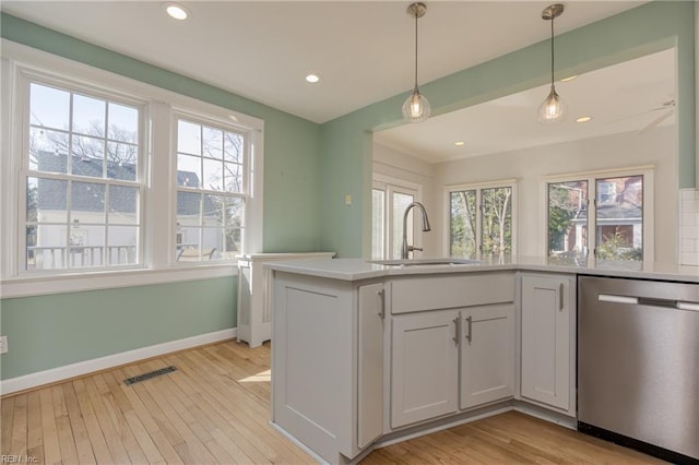 kitchen featuring visible vents, light wood-type flooring, a sink, stainless steel dishwasher, and baseboards