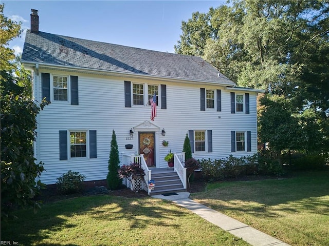 colonial home featuring a chimney and a front yard