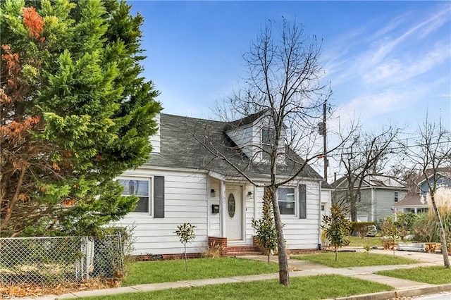 new england style home featuring entry steps, fence, a front lawn, and roof with shingles