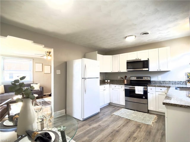 kitchen featuring appliances with stainless steel finishes, white cabinets, a sink, wood finished floors, and dark stone counters