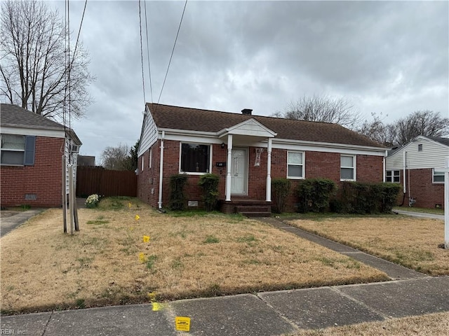 view of front of home featuring brick siding, fence, a front lawn, and roof with shingles