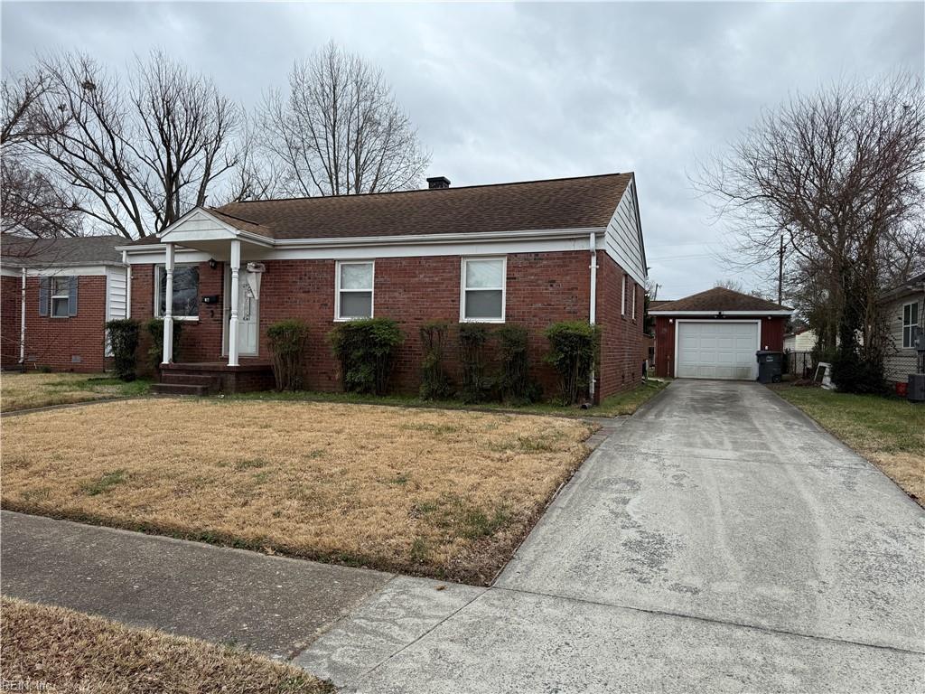 view of front of property with driveway, brick siding, a detached garage, an outbuilding, and a front yard