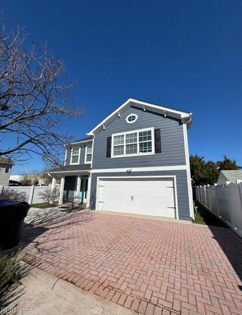 traditional-style house with a garage, decorative driveway, and fence