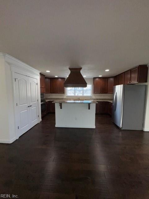 kitchen with premium range hood, dark wood-style flooring, a kitchen breakfast bar, light countertops, and freestanding refrigerator