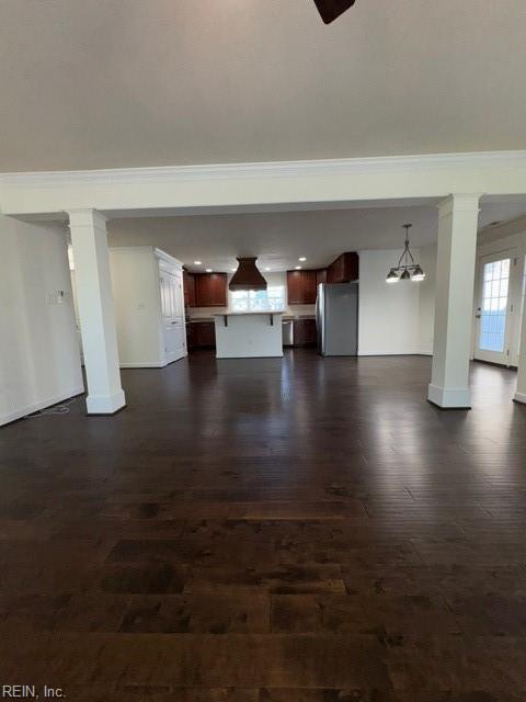 unfurnished living room featuring ornamental molding, dark wood-style flooring, decorative columns, and baseboards