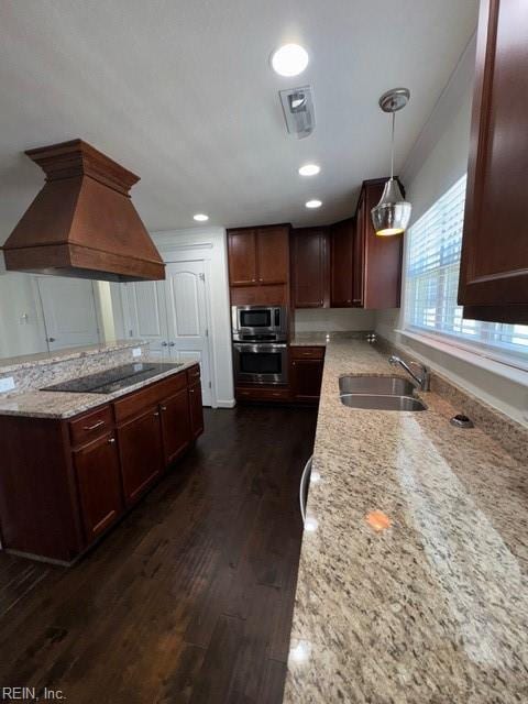 kitchen with dark wood-style floors, appliances with stainless steel finishes, light stone counters, premium range hood, and a sink