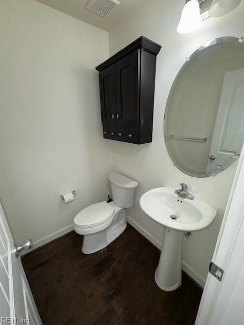 half bath with toilet, wood finished floors, visible vents, and baseboards