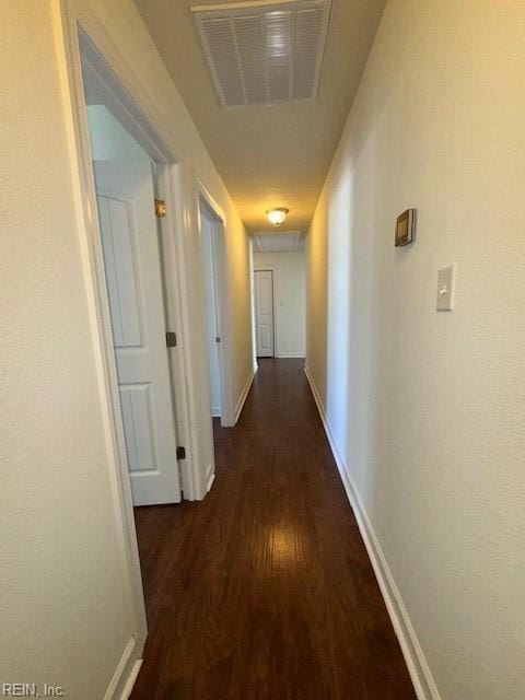 hall featuring dark wood-style flooring, visible vents, and baseboards