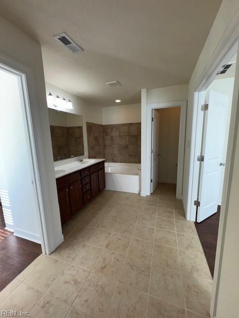 full bathroom with double vanity, a garden tub, baseboards, and visible vents