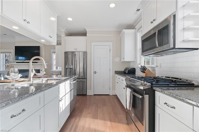 kitchen featuring light wood-style flooring, a sink, white cabinets, ornamental molding, and appliances with stainless steel finishes