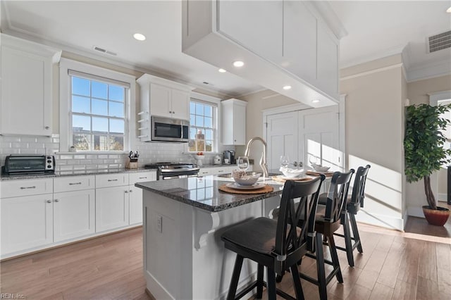 kitchen with appliances with stainless steel finishes, decorative backsplash, visible vents, and crown molding