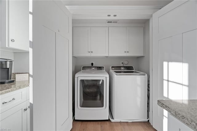 laundry room with visible vents, cabinet space, light wood finished floors, and washing machine and clothes dryer