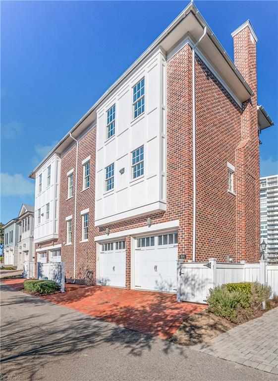 view of side of home featuring decorative driveway, brick siding, a chimney, and an attached garage