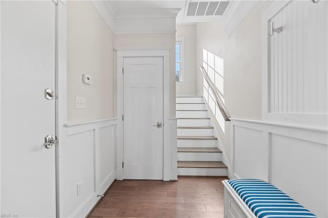 interior space featuring a decorative wall, wood finished floors, visible vents, wainscoting, and crown molding