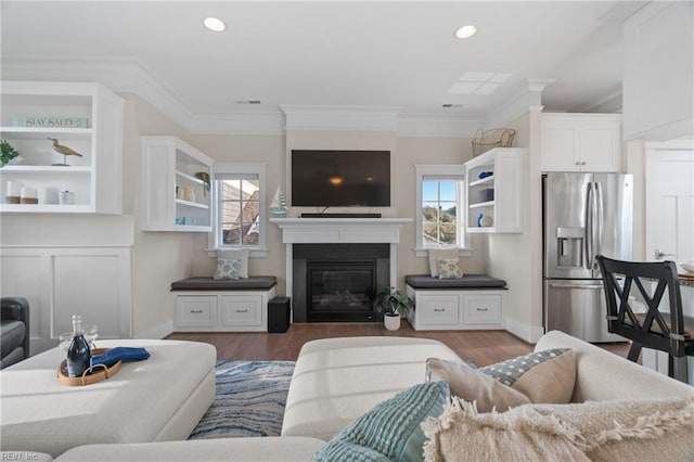 living area featuring a healthy amount of sunlight, visible vents, crown molding, and a glass covered fireplace