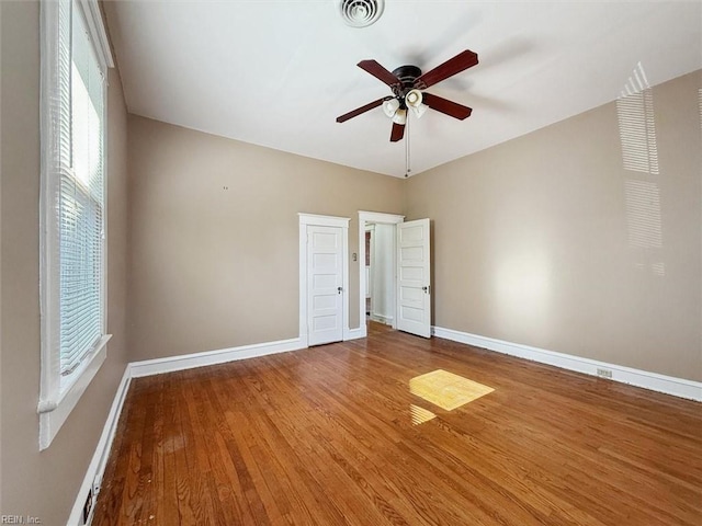 unfurnished room with ceiling fan, wood finished floors, visible vents, and baseboards