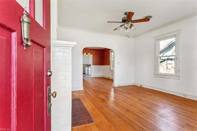 foyer entrance featuring arched walkways, crown molding, wood finished floors, a ceiling fan, and wallpapered walls