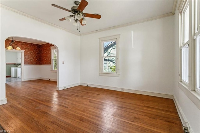 empty room with arched walkways, ceiling fan, ornamental molding, and wood finished floors