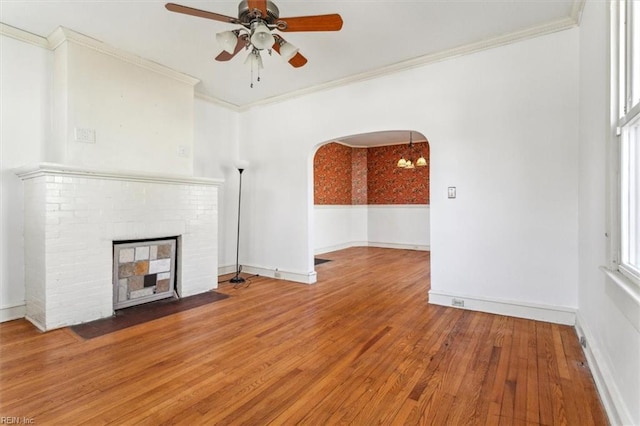 unfurnished living room featuring arched walkways, ornamental molding, a fireplace, and hardwood / wood-style flooring