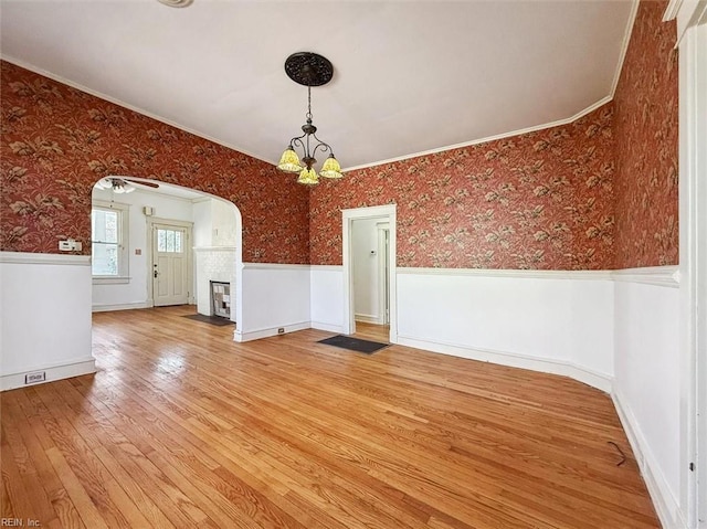 interior space featuring arched walkways, a wainscoted wall, a fireplace, light wood finished floors, and wallpapered walls