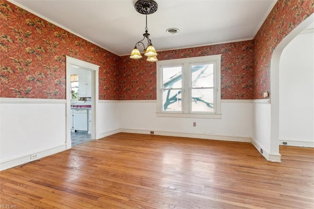 unfurnished dining area featuring arched walkways, a wainscoted wall, and wallpapered walls