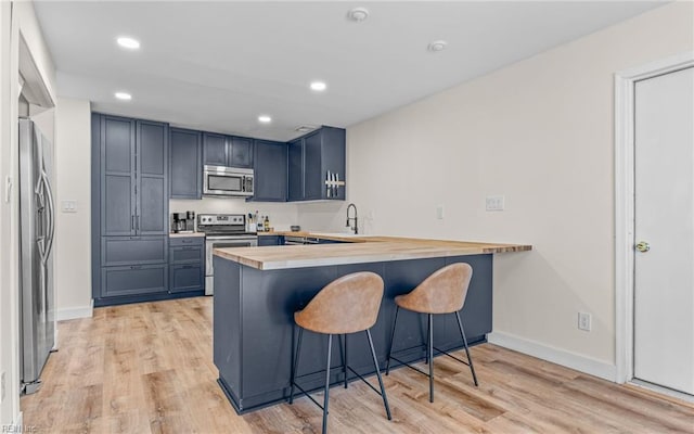 kitchen featuring butcher block counters, a breakfast bar area, a peninsula, stainless steel appliances, and light wood-type flooring