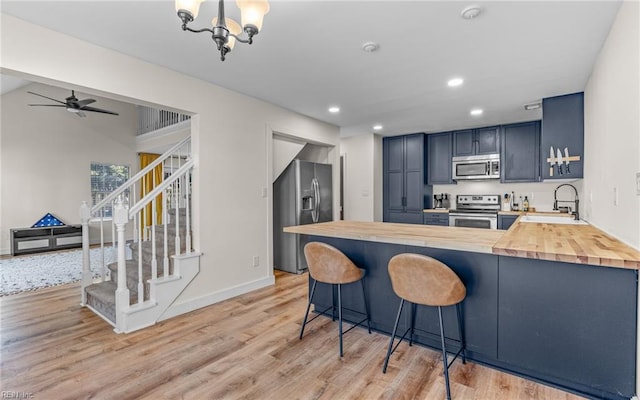 kitchen featuring appliances with stainless steel finishes, butcher block counters, a sink, and a peninsula