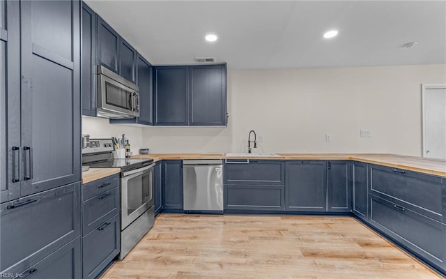 kitchen featuring stainless steel appliances, a sink, visible vents, light wood-style floors, and wooden counters