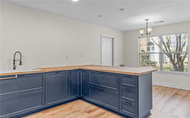 kitchen featuring light wood-style floors, wood counters, a sink, and an inviting chandelier