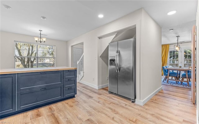 kitchen with decorative light fixtures, stainless steel fridge with ice dispenser, an inviting chandelier, light wood-type flooring, and baseboards