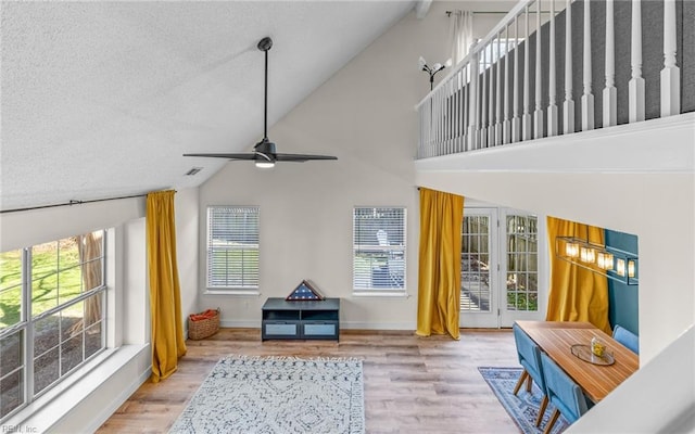 interior space with baseboards, a ceiling fan, wood finished floors, a textured ceiling, and high vaulted ceiling