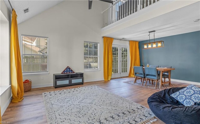 living area with high vaulted ceiling, wood finished floors, visible vents, and baseboards