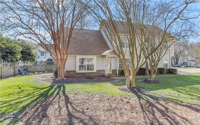 view of front of home featuring roof with shingles, brick siding, a front lawn, and fence