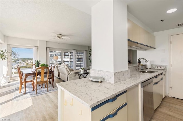 kitchen featuring a sink, light wood finished floors, dishwasher, and light stone countertops