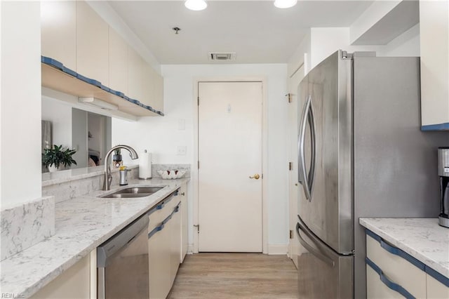 kitchen with stainless steel appliances, a sink, visible vents, light stone countertops, and light wood finished floors