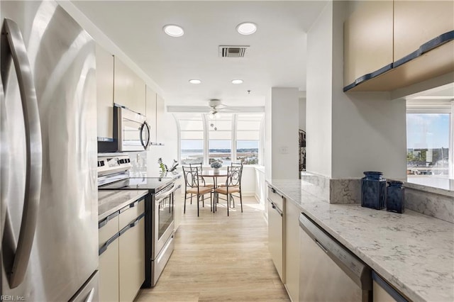 kitchen featuring light stone counters, stainless steel appliances, visible vents, ceiling fan, and light wood-type flooring