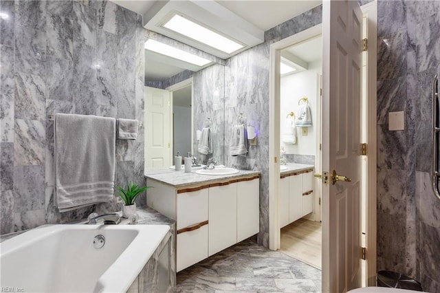 full bath with marble finish floor, vanity, a bath, and tile walls