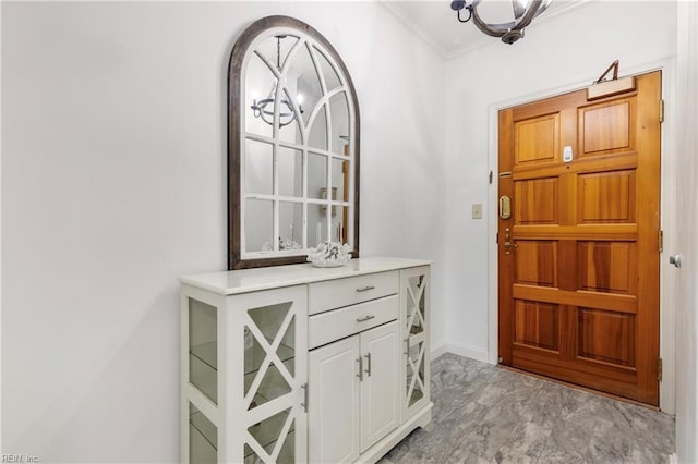 entryway featuring crown molding, a notable chandelier, and baseboards