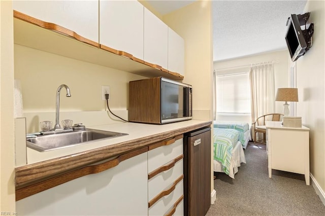 kitchen featuring carpet, light countertops, white cabinetry, a sink, and a textured ceiling