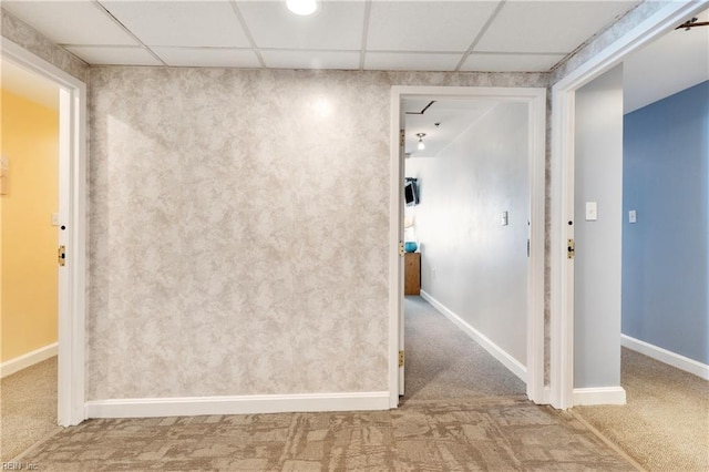 carpeted empty room featuring a drop ceiling and baseboards