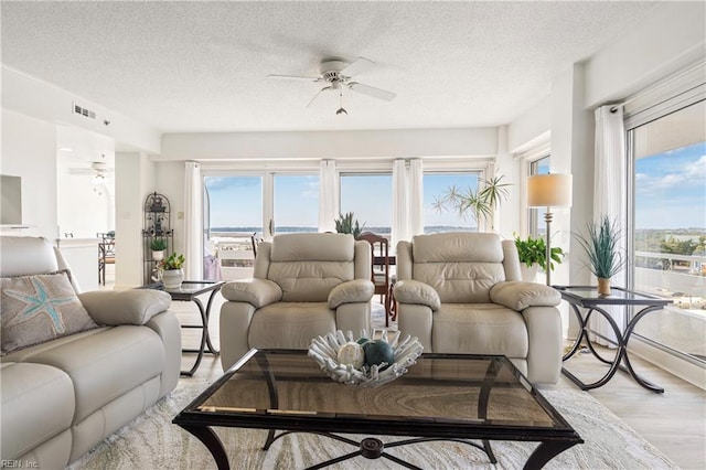 living area with visible vents, light wood-style flooring, a wealth of natural light, and a ceiling fan