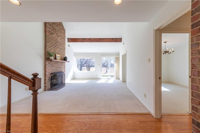 unfurnished living room featuring baseboards, stairway, an inviting chandelier, carpet, and a brick fireplace