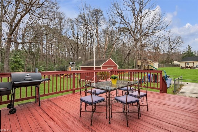 wooden deck featuring a playground, a lawn, outdoor dining space, a grill, and fence