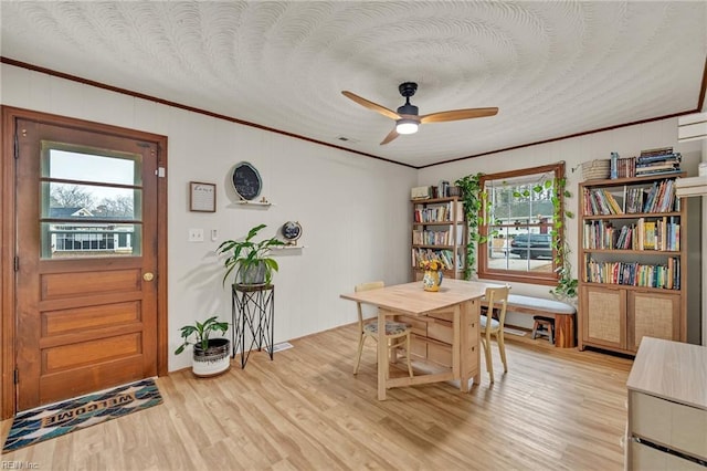 dining space featuring ornamental molding, light wood finished floors, a textured ceiling, and a ceiling fan