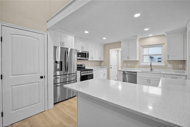 kitchen featuring light wood finished floors, appliances with stainless steel finishes, a sink, and white cabinets