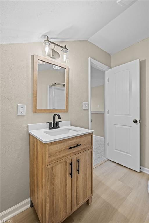 bathroom featuring vaulted ceiling, wood finished floors, vanity, and baseboards