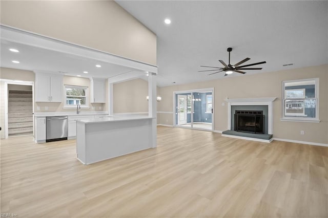 kitchen featuring light countertops, a fireplace with raised hearth, white cabinetry, ceiling fan, and dishwasher