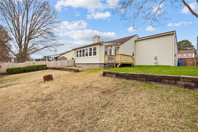 rear view of house featuring a deck, a lawn, a chimney, and fence