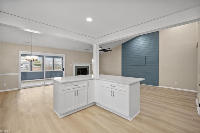 kitchen featuring a fireplace, light wood finished floors, open floor plan, white cabinetry, and ceiling fan with notable chandelier