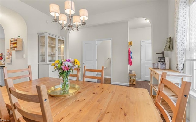 dining area with arched walkways, baseboards, wood finished floors, and a chandelier